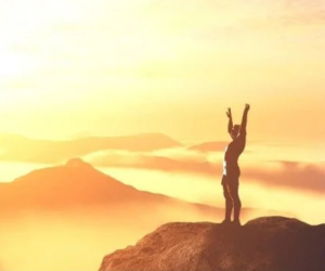 Person with arms raised on a mountain top at sunrise