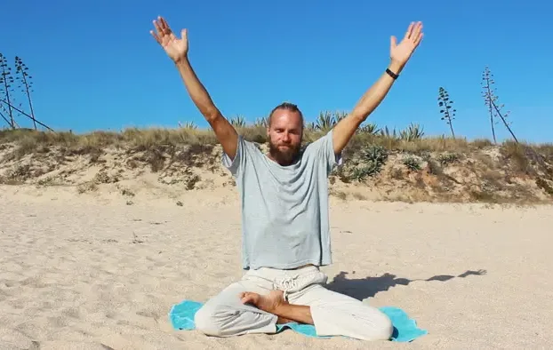 Michaël Bijker with arms raised in meditation on a beach in Portugal